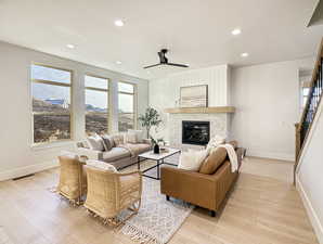 Living room with a fireplace, light hardwood / wood-style flooring, and ceiling fan