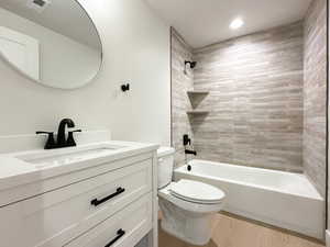 Full bathroom with hardwood / wood-style floors, vanity, tiled shower / bath combo, and toilet