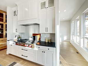 Kitchen featuring custom exhaust hood, backsplash, light hardwood / wood-style floors, white cabinetry, and stainless steel gas cooktop