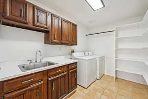 Washroom with cabinets, light tile patterned floors, washing machine and clothes dryer, and sink