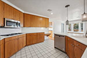 Kitchen featuring crown molding, sink, light tile patterned floors, appliances with stainless steel finishes, and decorative light fixtures