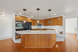 Kitchen with a large island, sink, hanging light fixtures, stainless steel appliances, and light wood-type flooring