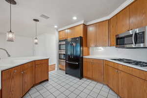 Kitchen featuring sink, appliances with stainless steel finishes, decorative light fixtures, light tile patterned flooring, and ornamental molding