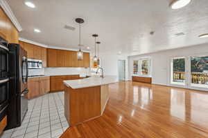 Kitchen featuring a center island with sink, ornamental molding, decorative light fixtures, light hardwood / wood-style floors, and stainless steel appliances