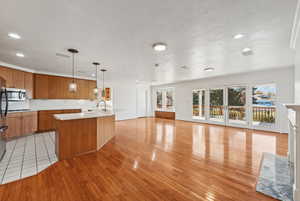 Kitchen featuring sink, hanging light fixtures, an island with sink, light wood-type flooring, and appliances with stainless steel finishes