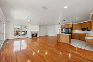 Kitchen with appliances with stainless steel finishes, crown molding, decorative light fixtures, a center island with sink, and light hardwood / wood-style floors