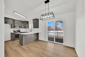 Kitchen with appliances with stainless steel finishes, decorative light fixtures, sink, light hardwood / wood-style floors, and kitchen peninsula