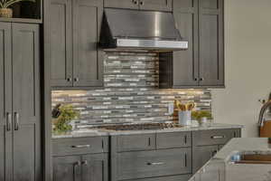 Kitchen with gray cabinetry, light stone countertops, and wall chimney exhaust hood