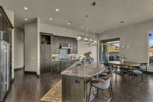 Kitchen featuring a kitchen island with sink, dark wood-type flooring, sink, hanging light fixtures, and decorative backsplash