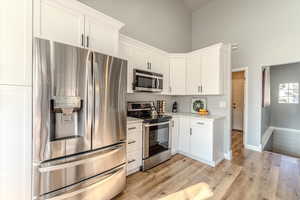 Kitchen with white cabinets, light hardwood / wood-style floors, a towering ceiling, and appliances with stainless steel finishes