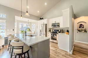 Kitchen featuring appliances with stainless steel finishes, light wood-type flooring, sink, decorative light fixtures, and white cabinetry