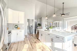 Kitchen featuring light wood-type flooring, stainless steel appliances, sink, high vaulted ceiling, and white cabinetry