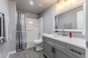 Full bathroom featuring shower / bath combo, vanity, a textured ceiling, hardwood / wood-style floors, and toilet