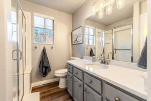 Bathroom featuring vanity, toilet, wood-type flooring, and a shower with door