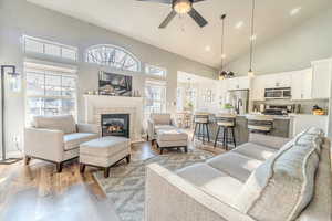 Living room with ceiling fan, light wood-type flooring, a fireplace, and high vaulted ceiling