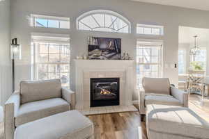 Living room with a tile fireplace, hardwood / wood-style floors, a healthy amount of sunlight, and an inviting chandelier