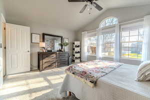 Carpeted bedroom featuring multiple windows, ceiling fan, and vaulted ceiling