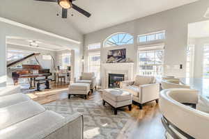 Living room with hardwood / wood-style floors, high vaulted ceiling, ceiling fan, and a tiled fireplace