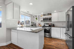 Kitchen featuring kitchen peninsula, stainless steel appliances, white cabinetry, dark stone counters, and sink