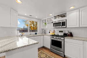 Kitchen featuring white cabinetry, sink, light stone counters, appliances with stainless steel finishes, and light wood-type flooring