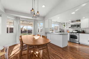 Kitchen with stainless steel appliances, white cabinets, decorative light fixtures, light stone countertops, and dark hardwood / wood-style floors