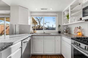 Kitchen featuring light stone counters, dark hardwood / wood-style floors, stainless steel appliances, white cabinetry, and sink