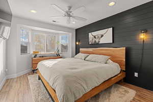 Bedroom featuring ceiling fan, light hardwood / wood-style floors, and wooden walls