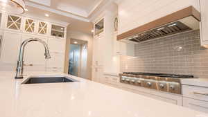 Kitchen featuring sink, tasteful backsplash, stainless steel gas stovetop, white cabinets, and custom range hood