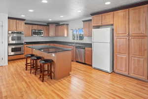 Kitchen with granite countertops, stainless steel appliances, light hardwood / wood-style floors, and a kitchen island