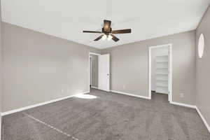 Unfurnished bedroom featuring dark colored carpet, ceiling fan, a spacious closet, and a closet