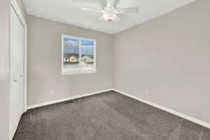 Unfurnished bedroom with ceiling fan, a closet, and dark carpet