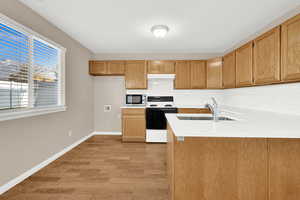 Kitchen with white range with electric stovetop, kitchen peninsula, sink, and light hardwood / wood-style flooring