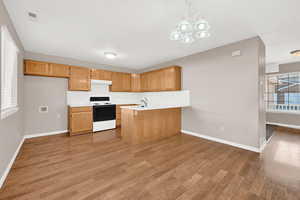 Kitchen featuring light hardwood / wood-style flooring, white electric stove, kitchen peninsula, decorative light fixtures, and decorative backsplash