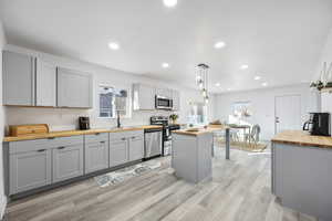 Kitchen featuring wooden counters, appliances with stainless steel finishes, gray cabinetry, decorative light fixtures, and a kitchen island