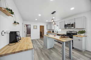 Kitchen with butcher block counters, sink, stainless steel appliances, light hardwood / wood-style floors, and decorative light fixtures