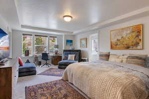 Bedroom with a raised ceiling, ensuite bathroom, and light colored carpet