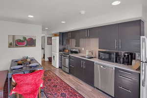 Kitchen with hardwood / wood-style flooring, stacked washer / dryer, sink, and appliances with stainless steel finishes