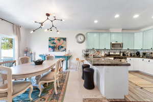 Kitchen with stainless steel appliances, dark stone countertops, a chandelier, decorative backsplash, and light wood-type flooring