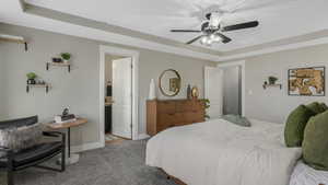 Carpeted bedroom featuring ensuite bath, a raised ceiling, and ceiling fan