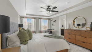 Bedroom with ceiling fan, a raised ceiling, light colored carpet, and ensuite bathroom