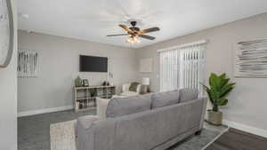 Living room with ceiling fan and dark wood-type flooring