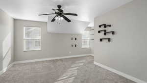 Carpeted spare room with plenty of natural light, ceiling fan, and vaulted ceiling