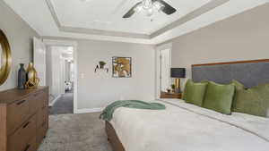 Carpeted bedroom with a tray ceiling and ceiling fan