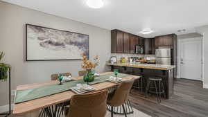 Kitchen featuring decorative backsplash, appliances with stainless steel finishes, a breakfast bar, dark brown cabinetry, and dark wood-type flooring