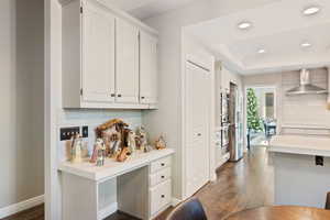 Kitchen with backsplash, a raised ceiling, wall chimney range hood, dark hardwood / wood-style flooring, and white cabinetry