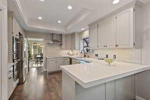 Kitchen with white cabinets, sink, wall chimney exhaust hood, dark hardwood / wood-style floors, and kitchen peninsula