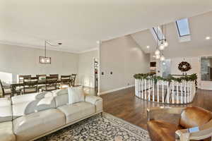 Living room featuring crown molding, vaulted ceiling with skylight, and dark wood-type flooring