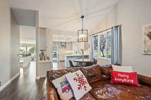 Living room featuring lofted ceiling, dark hardwood / wood-style flooring, a healthy amount of sunlight, and a notable chandelier