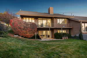 Back house at dusk featuring a balcony, a yard, and a patio