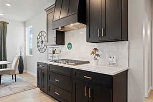 Kitchen featuring backsplash, light hardwood / wood-style floors, stainless steel gas stovetop, and custom exhaust hood